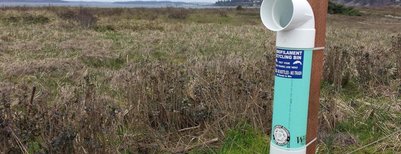 White monofilament tube tied to post with scenic field and water in background at Fort Worden State Park