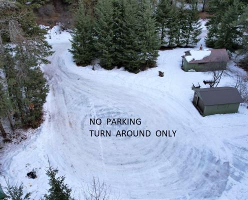 A cul-de-sac covered by compacted thin ice and snow labeled with the words "NO PARKING TURN AROUND ONLY", with two small building structures and surrounded by trees.