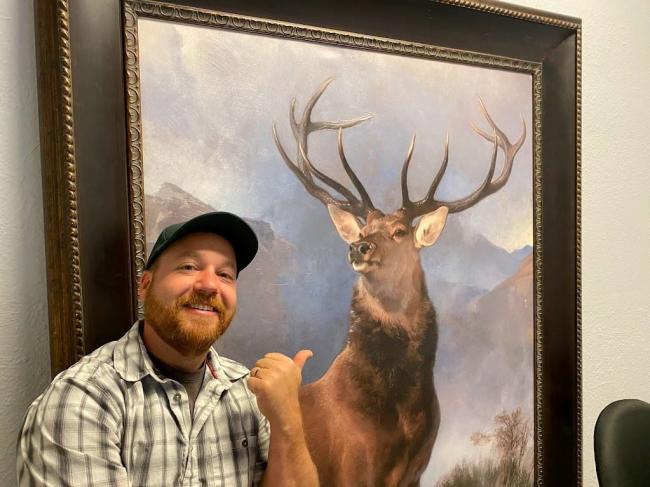 Man smiles and points to painting of a large buck