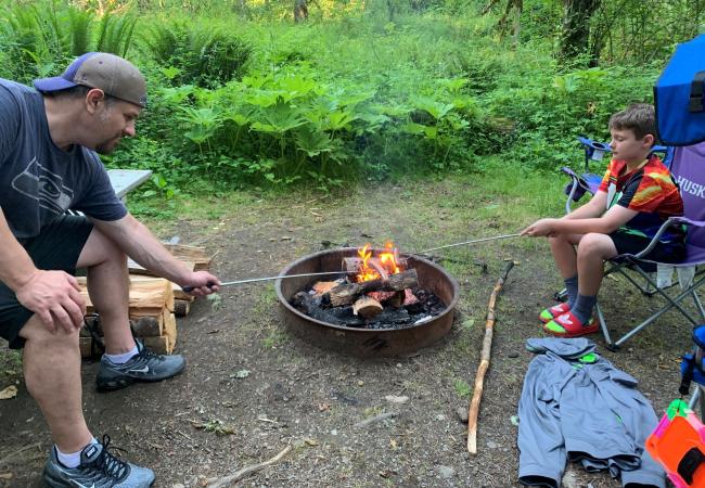 Father and son grill hot dogs over a campfire