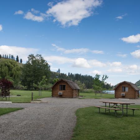 Three log cabins at the end of a gravel road on the edge of a lake.