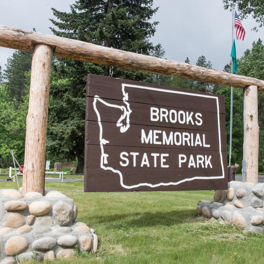 Large brown state park sign hanging from wooden round beams and concrete and stone base on green grass