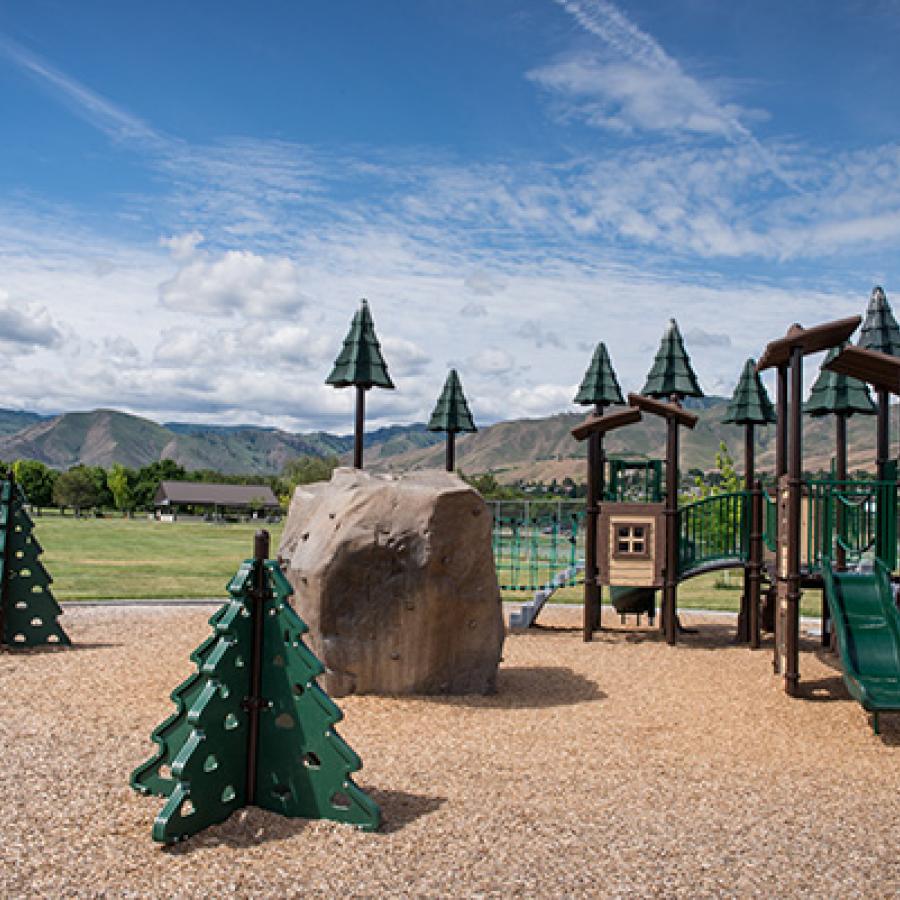 An outdoor children's play area with toys shaped like rocks and evergreen trees.