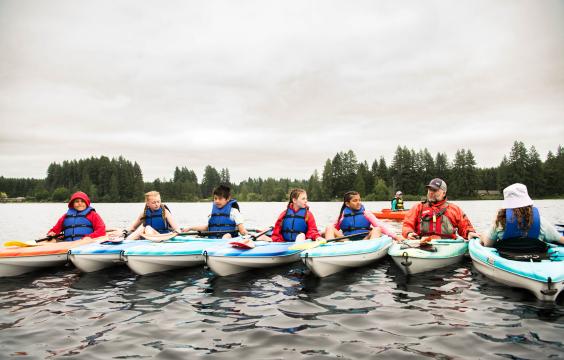 young participants in a kayak safety course on the water, all wearing lifejackets