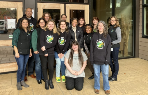 A group of people who work for the Washington State Parks human relations department posing in front of wood and glass entrance doors to the Park's headquarters building.