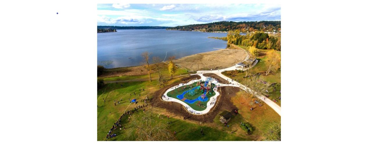 Aerial view Lake Sammamish with playground, bath house along walking path in the foreground, to the right are trees.
