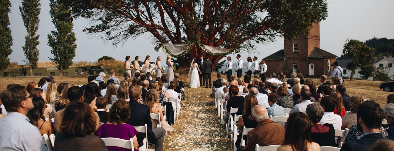 Outdoor wedding at Fort Worden State Park in front of a madrona tree and castle.