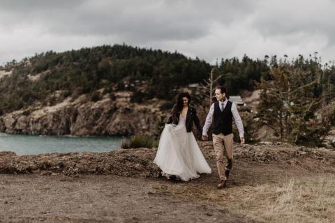 A bride and groom walk amidst basalt cliffs with the sea in the background.
