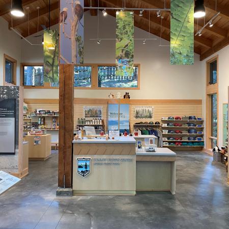 Inside the visitor center, a wood beam sits in the middle of concrete floors with a sales desk made of light colored wood and the State Park emblem on the front. Merchandise and displays line the building walls.