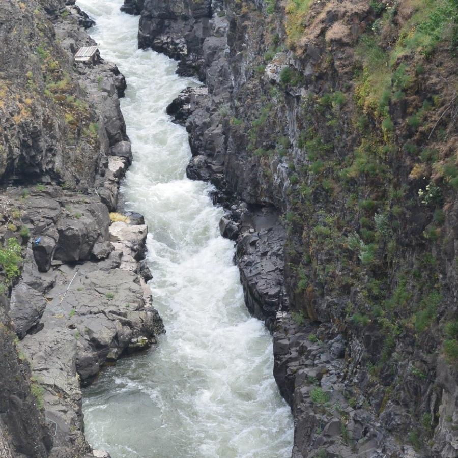 A narrow river with rapids runs along the bottom of a narrow rocky canyon.