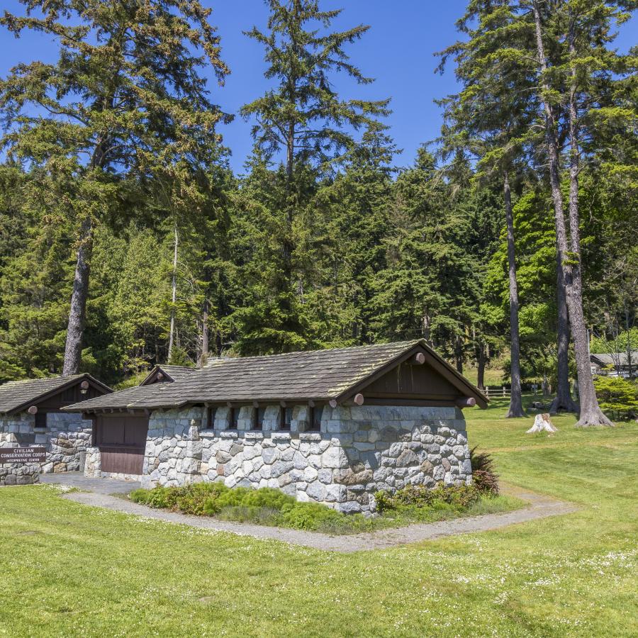 The rock interpretive building sits on a green lawn with tall, green trees and a blue sky behind it