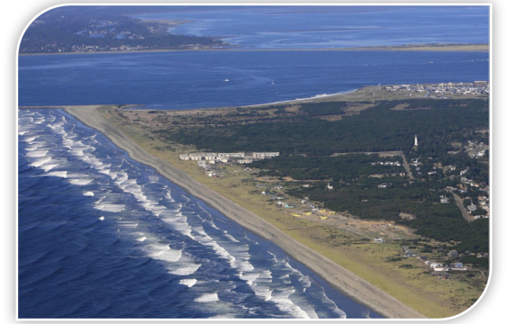 Aerial view of the Westport Light Park point. Left is the ocean with white cape waves. Right is the beach, and trees and some buildings right of that.
